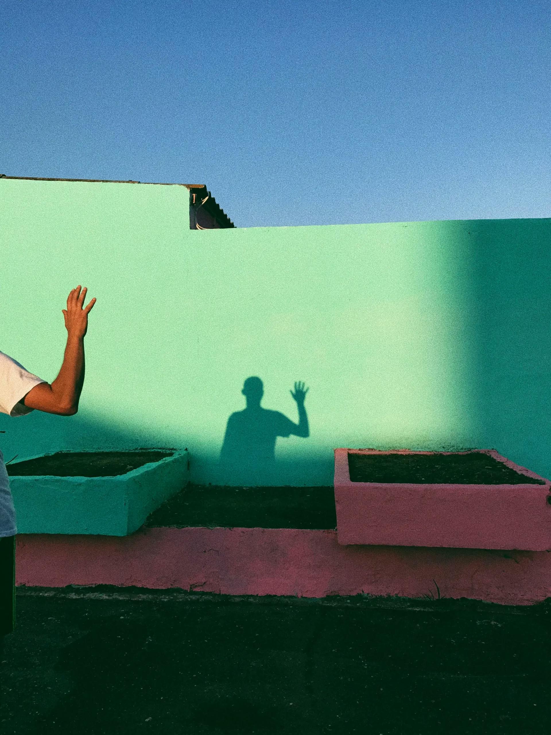 Shadow of a person waving against a colourful wall,